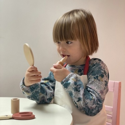 Criança aplicando batom enquanto se olha num espelho redondo de madeira