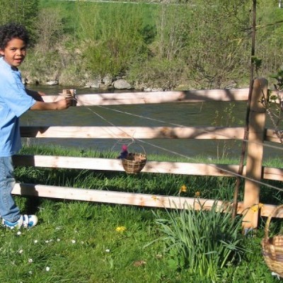 Criança a usar dispositivo de madeira para transportar cesto suspenso junto a cerca de madeira