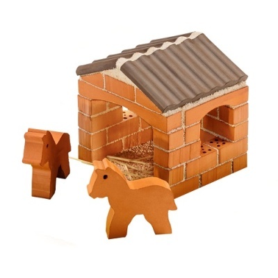 Casa de brincar em tijolos laranja com telhado cinza e duas figuras de cavalos em madeira laranja