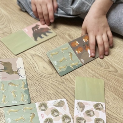 Cartas de jogo infantil com desenhos de animais e mãos de criança num chão de madeira