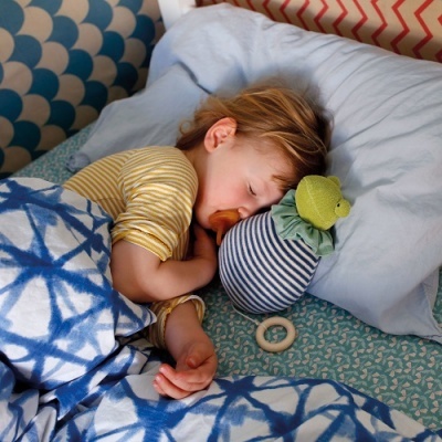 Criança a dormir com brinquedo e lençóis azuis e brancos