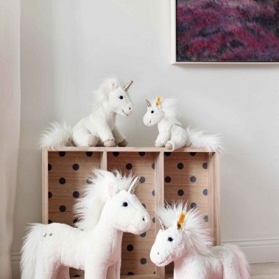 Peluches de unicórnio brancos com crinas felpudas colocados em prateleira e tapete
