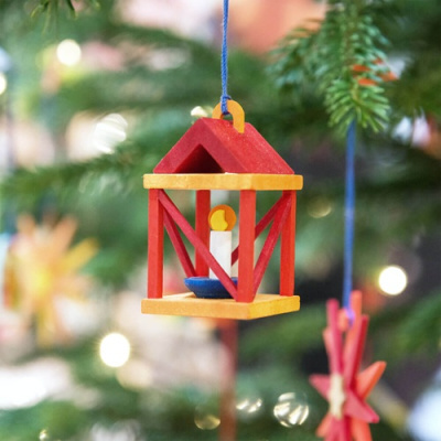 Lanterna decorativa vermelha e amarela com vela pendurada numa árvore de Natal