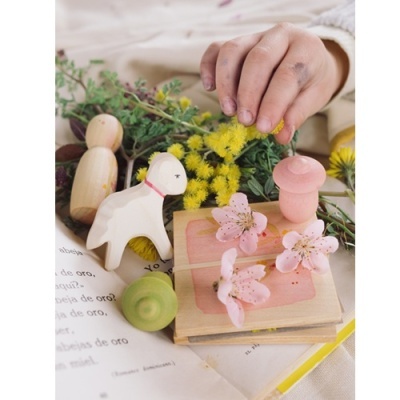 Brinquedos de madeira pintados e flores sobre livro aberto com mão infantil ao fundo