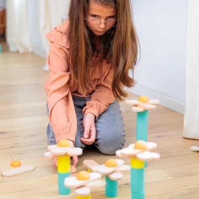 Menina a jogar com brinquedos de madeira em forma de flores coloridas num chão de madeira
