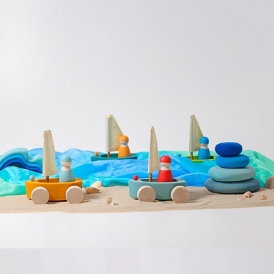 Brinquedos de barcos de madeira coloridos sobre tecido azul e bege com pedras empilhadas