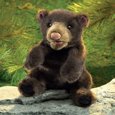 Urso de peluche castanho sentado numa pedra com vegetação verde ao fundo