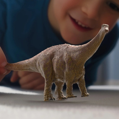 Dinossauro de brinquedo castanho claro com criança atrás