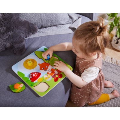 Criança a brincar com puzzle de madeira colorido sobre sofá cinzento