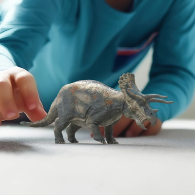 Brinquedo de dinossauro Tricerátopo cinzento com manchas alaranjadas sobre fundo branco