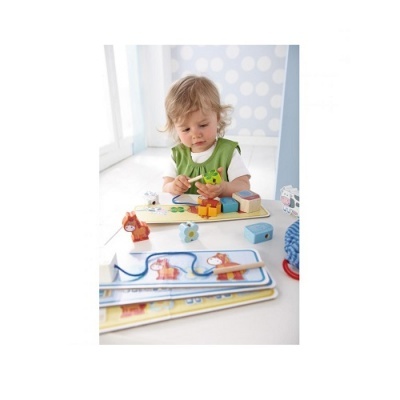 Criança a brincar com brinquedos de madeira coloridos e livros infantis numa mesa branca