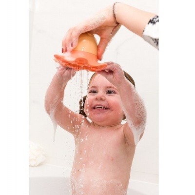 Criança na banheira a brincar com copo laranja e espuma de banho