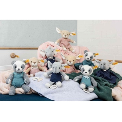 Peluches de coelho, panda e elefante em tecidos macios coloridos sobre mantas num cenário interior