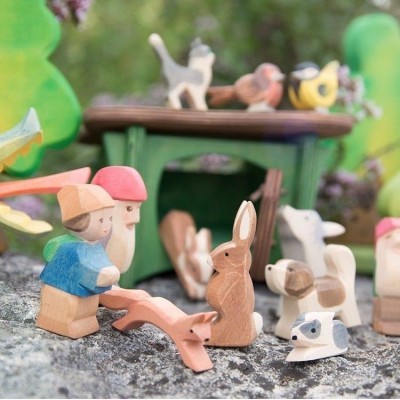 Brinquedos de madeira pintada com figuras humanas e animais, mesa verde com pássaros, em superfície rochosa