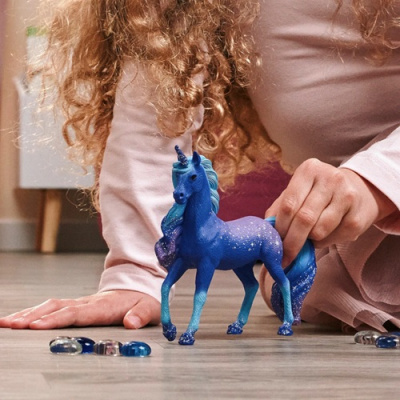 Brinquedo de unicórnio azul em chão de madeira com pedras coloridas