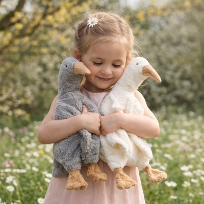 Menina abraçando dois peluches em forma de patos, cinzento e branco, num campo florido