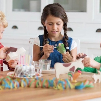 Três crianças a pintar animais de madeira numa mesa interior