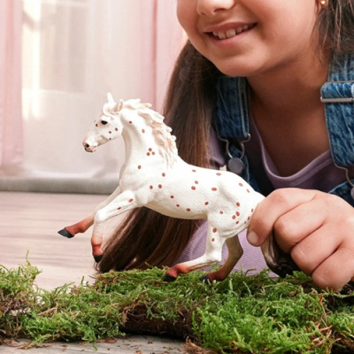 Cavalo de brinquedo branco com manchas castanhas e criança a brincar