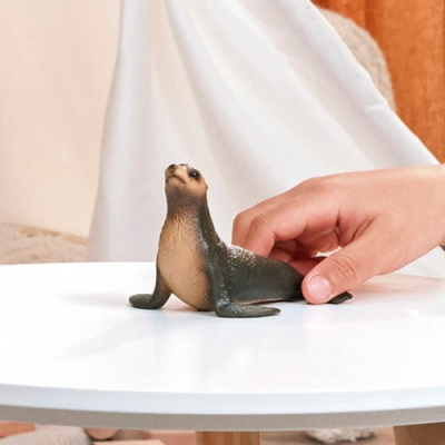 Miniatura realista de uma foca castanha e preta sobre mesa branca com mão ao lado