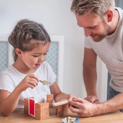 Criança e adulto a brincar com bloco tipo tijolo castanho e uma porta vermelha numa mesa