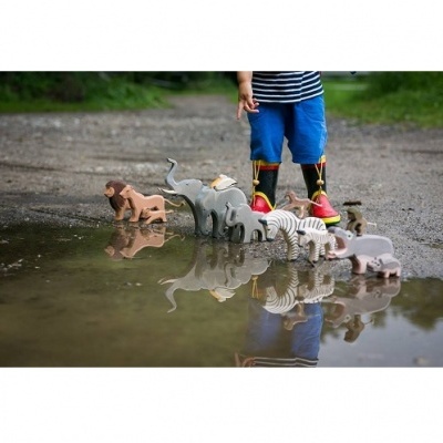 Brinquedos de animais de madeira refletidos numa poça de água com menino ao fundo usando botas de chuva