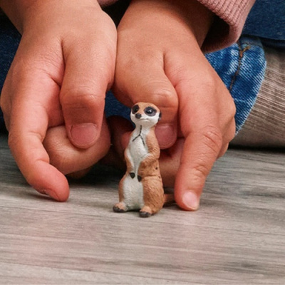 Figura pequena de suricata com mãos infantis ao redor