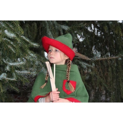 Criança com chapéu e capa verde e vermelha perto de árvore