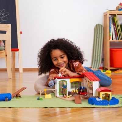 Criança a brincar com casinha de brinquedo em madeira colorida num tapete verde