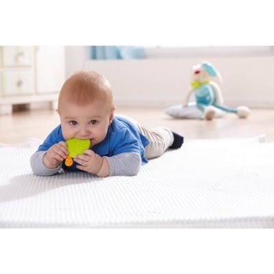 Bebé deitado no tapete a morder brinquedo amarelo e verde.