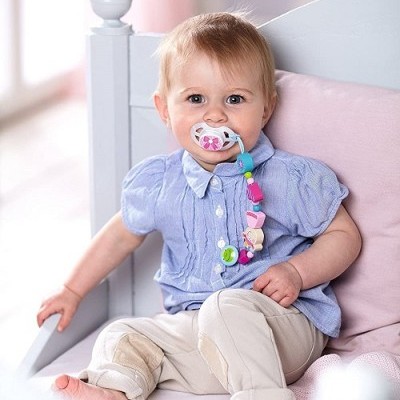 Bebé sentado em cadeira branca usando chucha colorida e roupa azul e bege