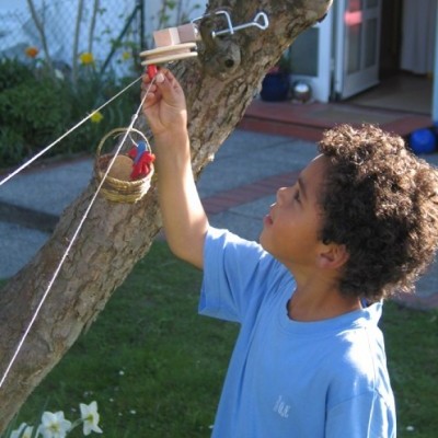 Criança a brincar com brinquedo artesanal pendurado numa árvore num jardim