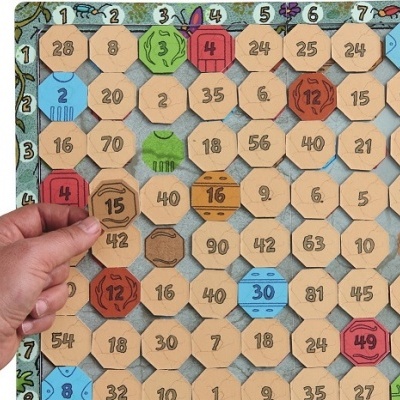 Tabuleiro de jogo com peças hexagonais numeradas coloridas e mão segurando uma peça.