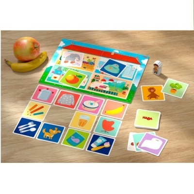 Jogo de cartas infantil colorido da HABA com tabuleiro, figura de madeira, banana e maçã sobre mesa de madeira