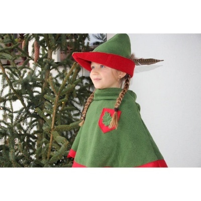Menina com capa verde e vermelha e chapéu pontudo com pena junto a árvore de Natal
