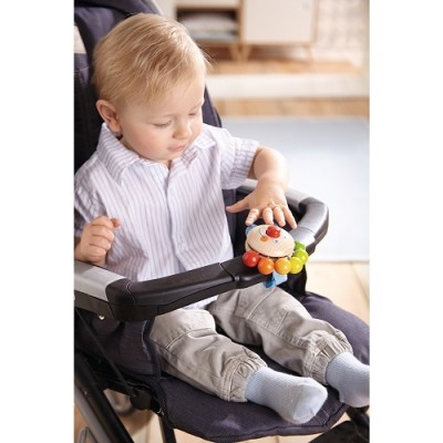 Bebé num carrinho cinzento a tocar num brinquedo colorido com rosto sorridente.