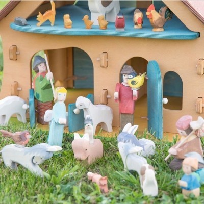 Casinha de madeira com figuras de animais e pessoas pintadas em madeira sobre relva