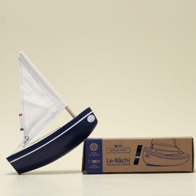 Barco de madeira azul com vela branca e embalagem de cartão castanho com texto azul.