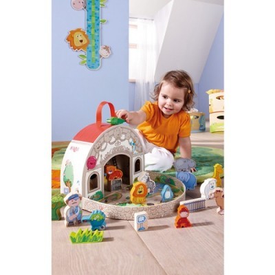 Menina a brincar com uma casa de madeira de brincar e figuras de animais em ambiente interior infantil