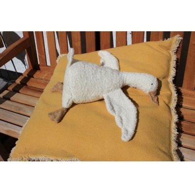 Peluche de pato branco sobre almofada amarela com franjas numa cadeira de madeira