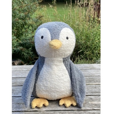 Pelúcia de pinguim cinzenta e branca com bico e patas amarelos numa mesa de madeira ao ar livre