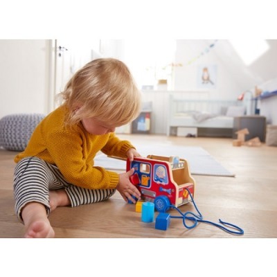 Criança brincando com brinquedo de autocarro de madeira colorido em quarto