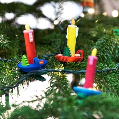 Três velas coloridas com suportes decorados penduradas em árvore de Natal verde