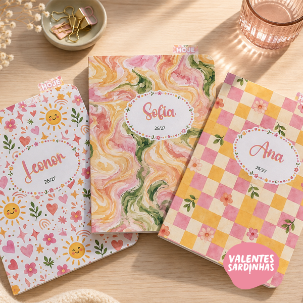 Planner'26 | Happy Days Três cadernos coloridos com padrões florais e geométricos e nomes nas capas, sobre mesa clara com clips e copo rosa