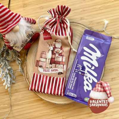 Saco de pano natalício e barra de chocolate Milka sobre prato de madeira