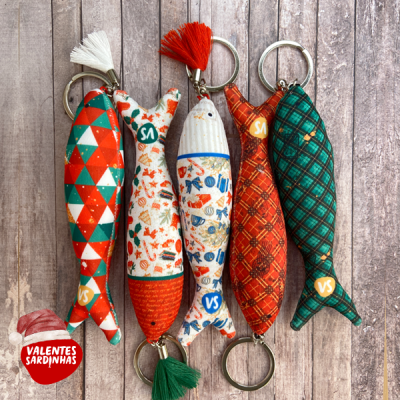 Cinco porta-chaves de sardinha de tecido coloridos com padrões variados sobre madeira envelhecida