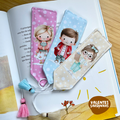Três marcadores de livros coloridos em tecido com imagens de crianças e pompons