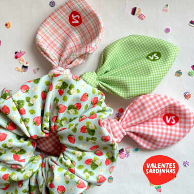 Três scrunchies coloridos com laços e padrão de morangos e xadrez sobre fundo branco com adesivos coloridos