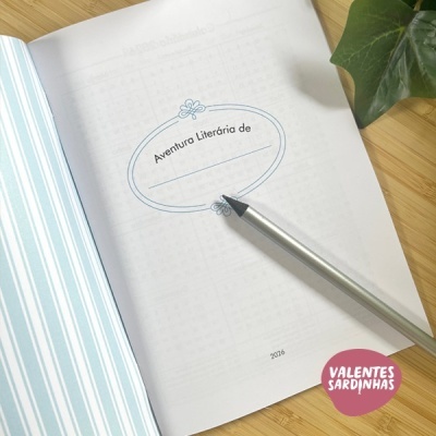 Caderno aberto com texto Aventura Literária de e caneta sobre página