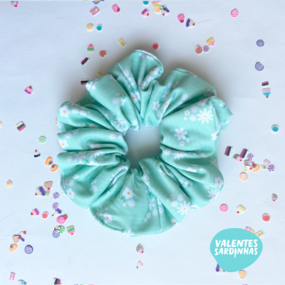 Elástico de cabelo verde água com flores brancas sobre fundo branco com confetes coloridos