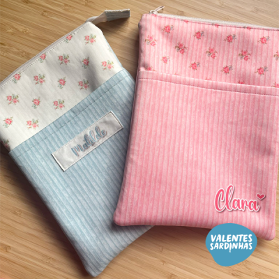Duas bolsas de tecido azul claro e rosa com padrões florais e etiquetas com nomes